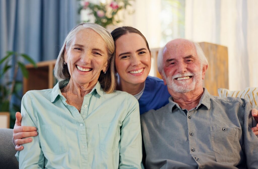 A woman caretaker smiling and sitting on a couch with an older couple in a senior living community.