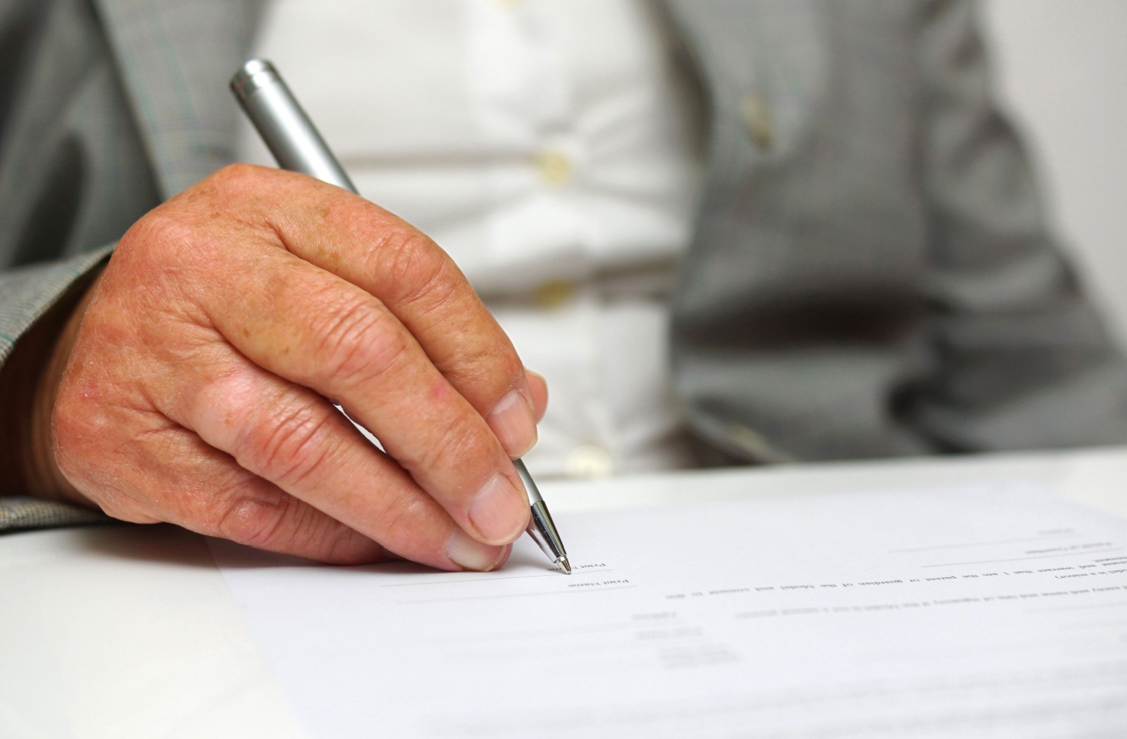 An older adult man signing legal documents.