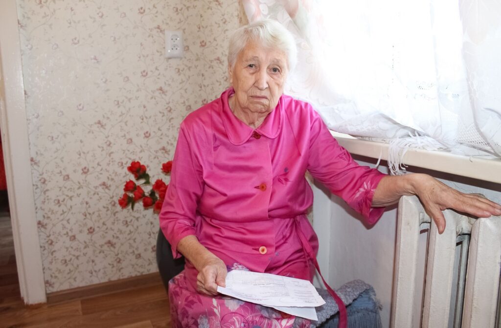 Older adult woman sitting in a chair in a senior living community holding legal documents.