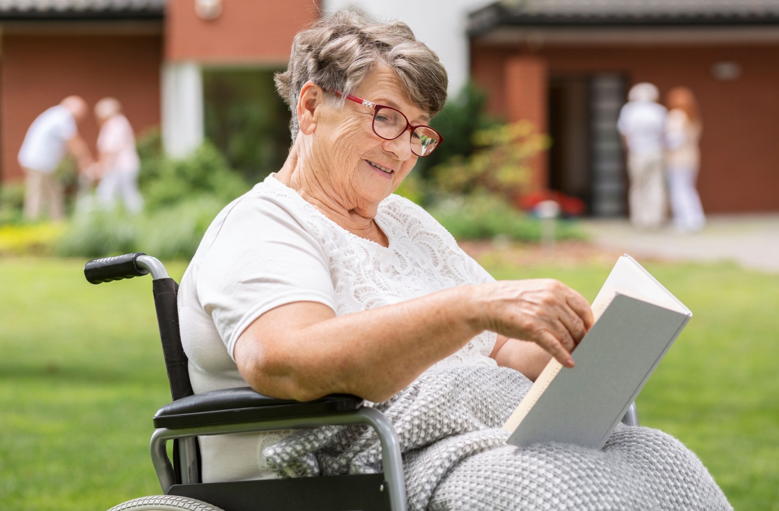 A senior who uses a wheelchair enjoying a book in the community garden at an assisted living community