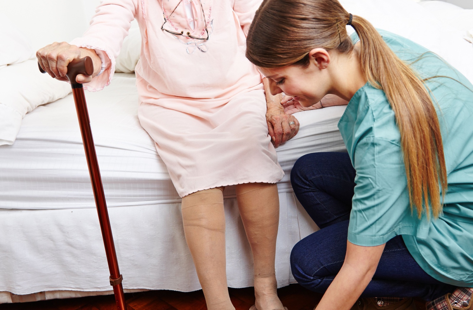 An assisted living caregiver helps a senior woman put on her shoes.