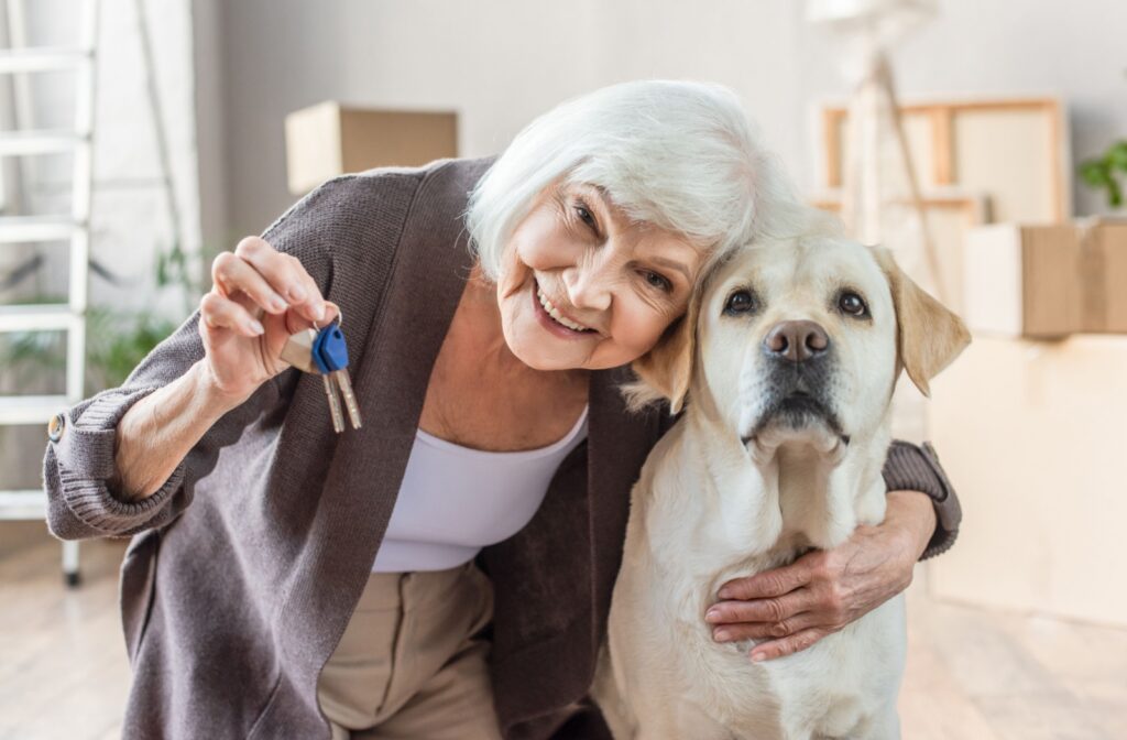 A senior woman hugs her dog while holding up a pair of keys to her assisted living apartment.