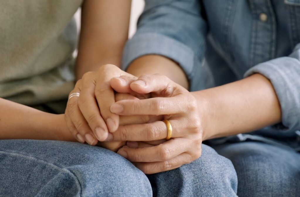Close-up of two people in casual clothes holding hands gently offering comfort and emotional support during a quiet moment