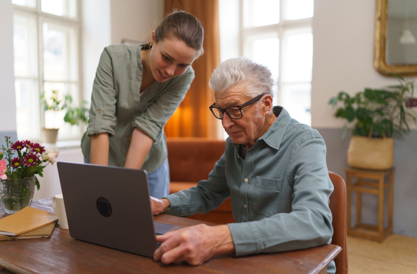 A caregiver helping a senior man learn how to use his laptop.