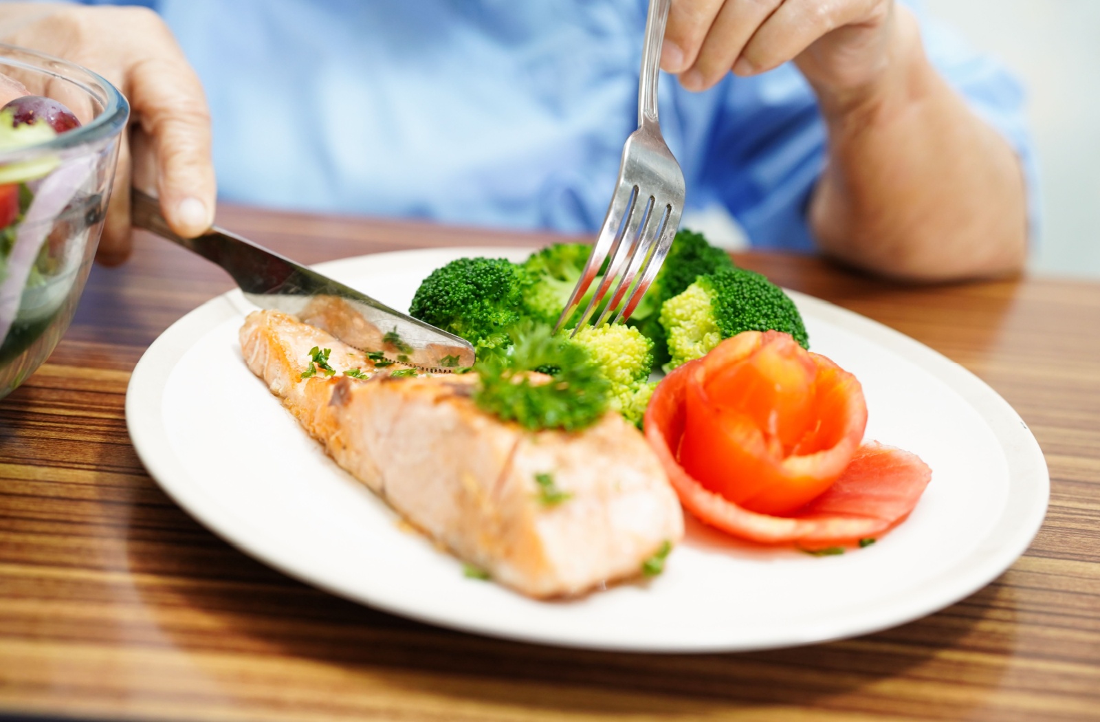 A close-up image of a senior enjoying a balanced meal that includes fish and vegetables.