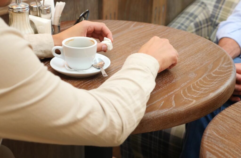 Close-up of the hands of a senior and their adult child having coffee together while discussing future care options.