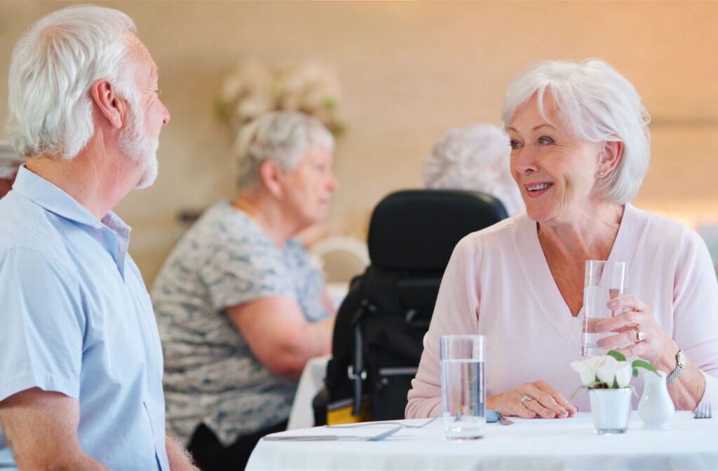 An older couple smiles at one another while waiting for their meal in an assisted living dining area