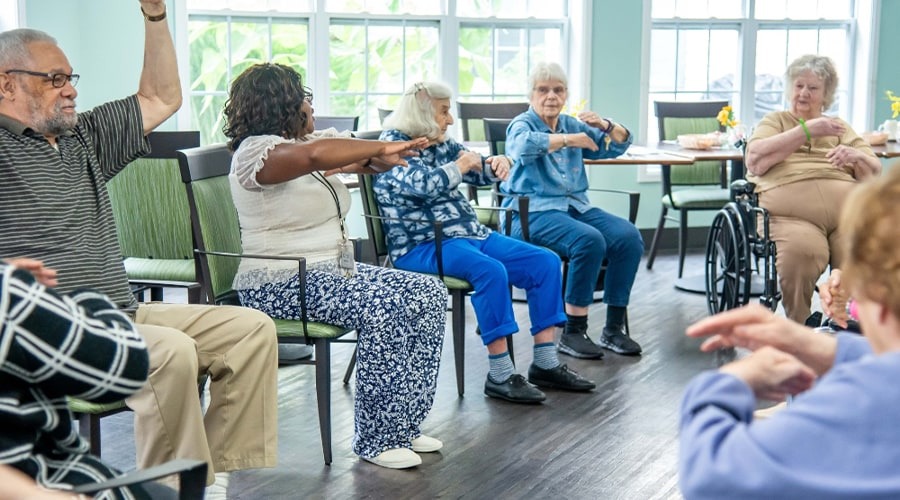 A group of seniors performing chair exercises at a senior living community.