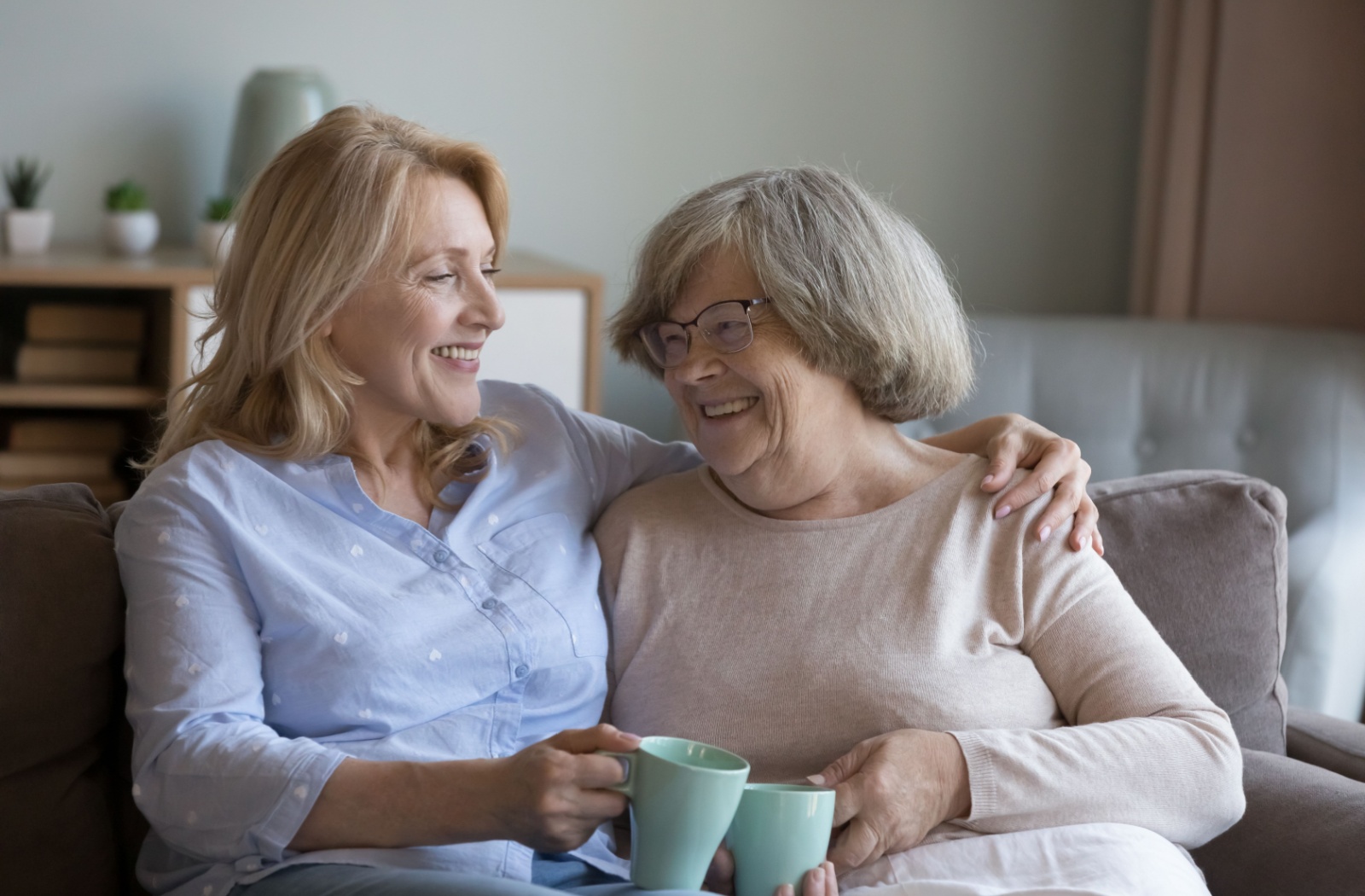 An adult wraps their arm around their older parent’s shoulders during a conversation about senior living over tea