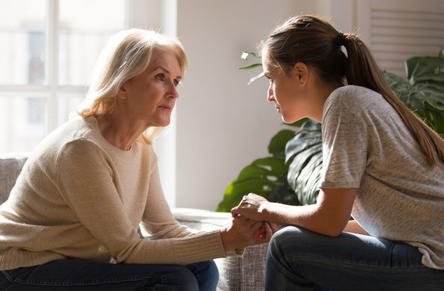 A young adult clasps their older parent's hands during a heartfelt discussion about assisted living