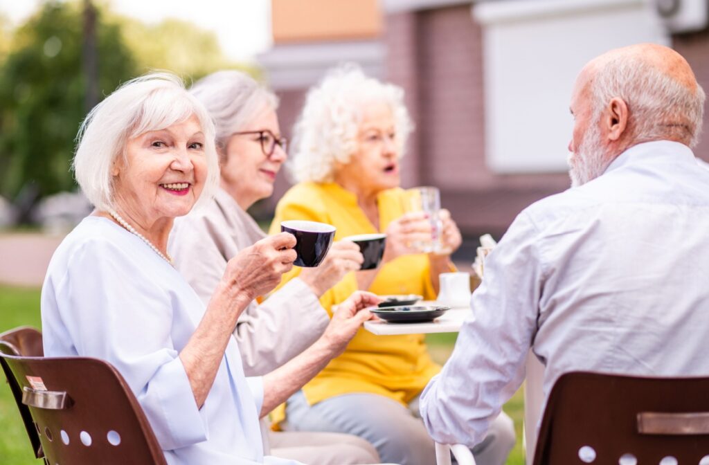 A group of seniors sits outside in assisted living, enjoying hot beverages.