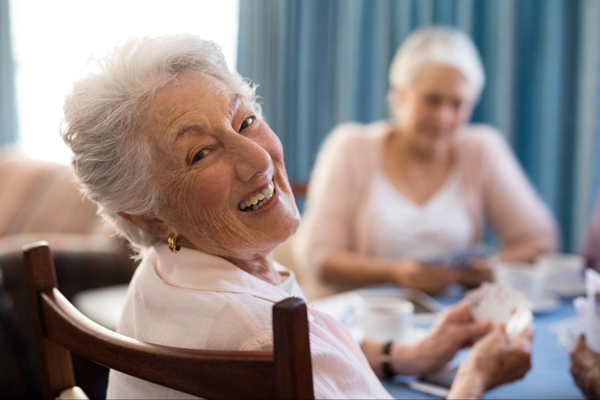a senior looking at camera and smiling while playing card games in an assisted living community